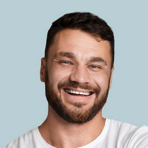 Professional headshot of a man with short dark hair and a trimmed beard, wearing a white shirt, smiling broadly against a soft teal background.