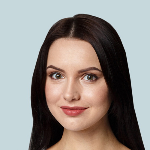 Professional headshot of a woman with long dark hair, wearing a natural makeup look, smiling subtly against a soft light blue background.